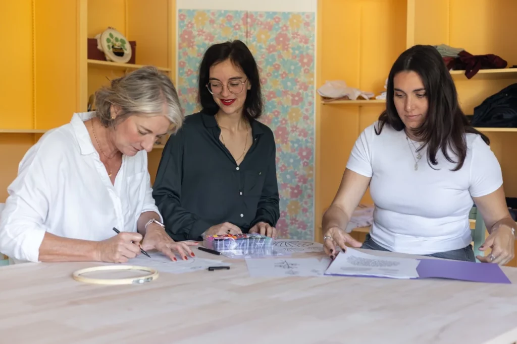 Julie artisane brodeuse dans son atelier qui accompagne deux élèves lors d'un atelier d'initiation à la broderie main