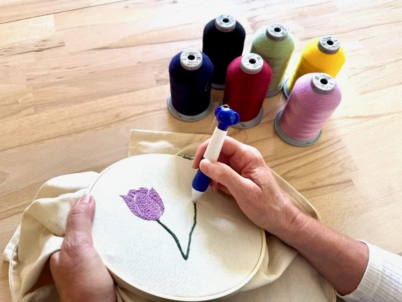 Main tenant l'aiguille spécifique à l'atelier d'initiation à la broderie texturée ainsi que des bobines de fils à laine