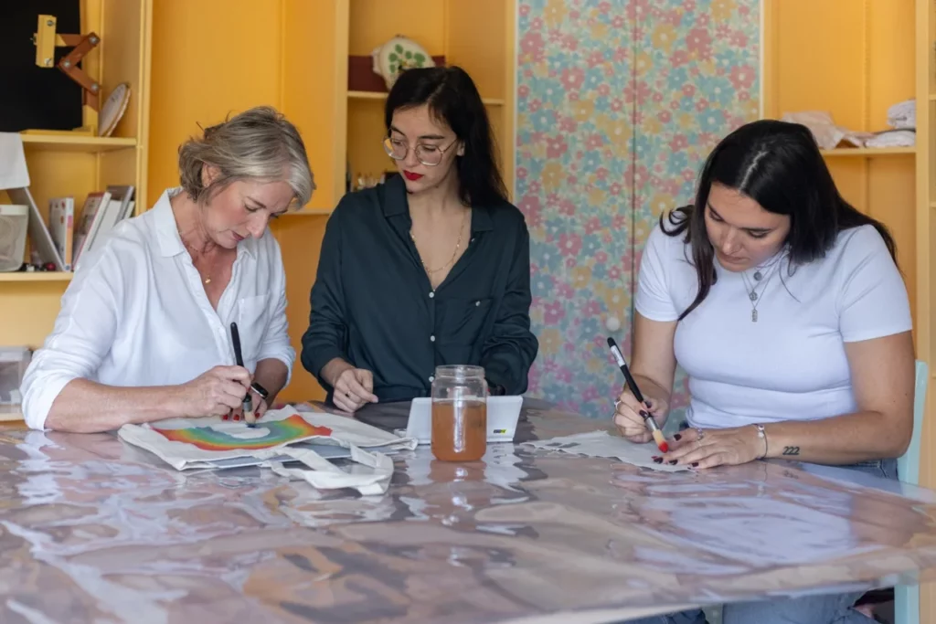 Julie artisane brodeuse à mérignac qui accompagne deux participantes lors d'un atelier d'initiation à l'aquarelle sur textile et broderie à la main
