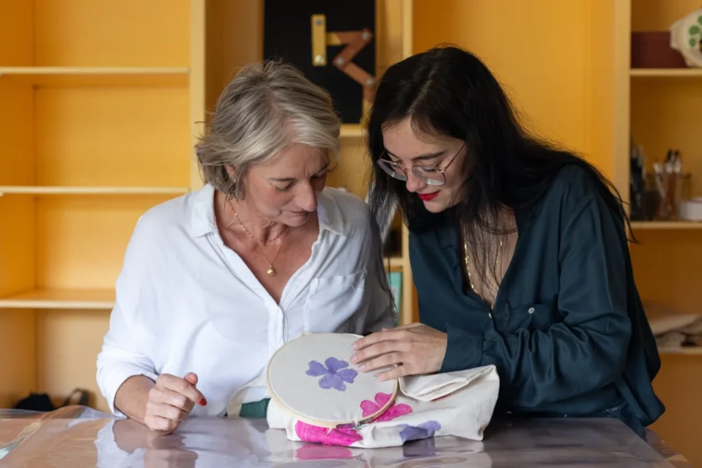 Julie artisane brodeuse qui explique à une élève des points de broderie à la main lors d'un atelier créatif
