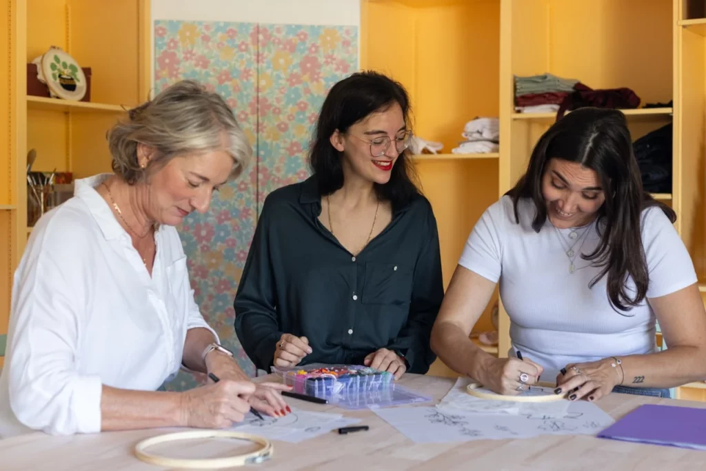 Julie artisane brodeuse qui accompagne deux élèves lors d'un atelier créatif de broderie à la main