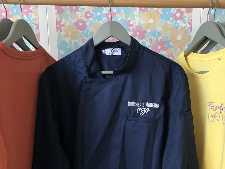 Veste de cuisine bleu brodé avec le nom d'une entreprise sur le coeur