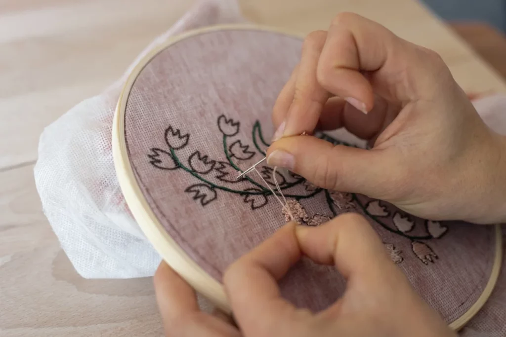 Gros plan d'une main en train de faire de la broderie à la main lors d'une atelier d'initiation
