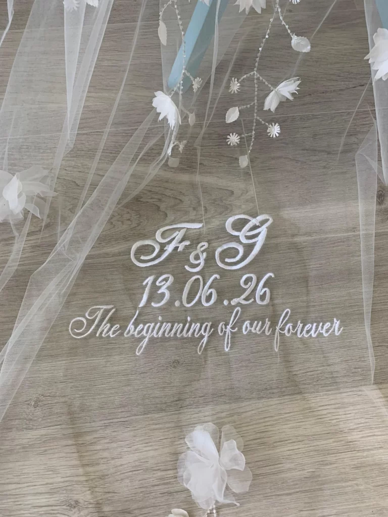 Gros plan sur une broderie de date, initiales et citations faite sur un voile de mariée