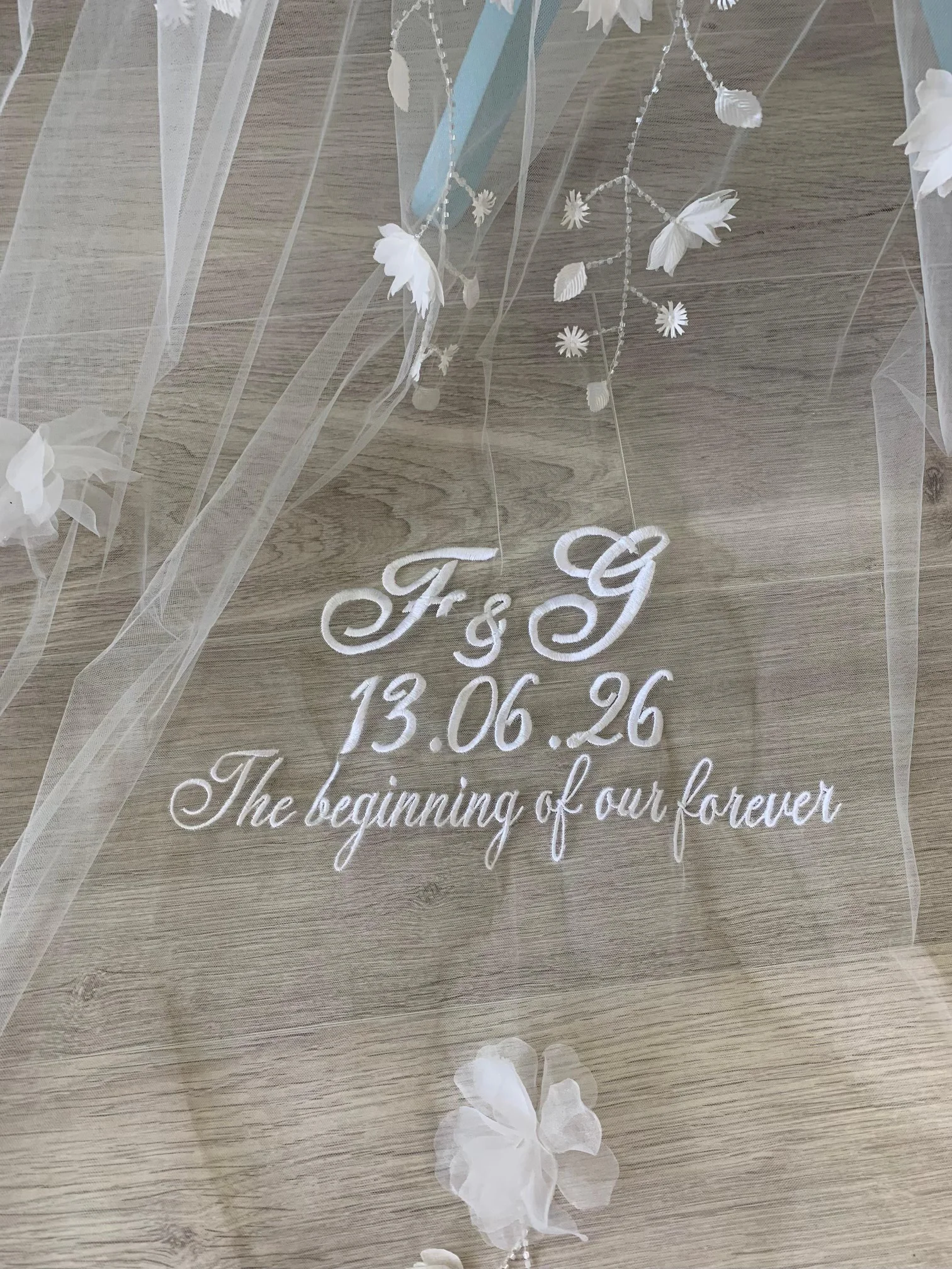 Gros plan sur une broderie de date, initiales et citations faite sur un voile de mariée