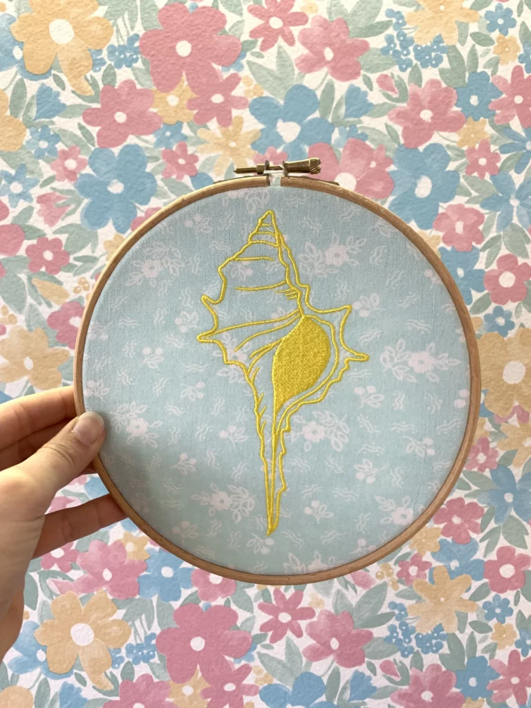 Broderie d'un coquillage jaune sur un tissu de seconde main bleu fleuri, décoration intérieure en pièce unique