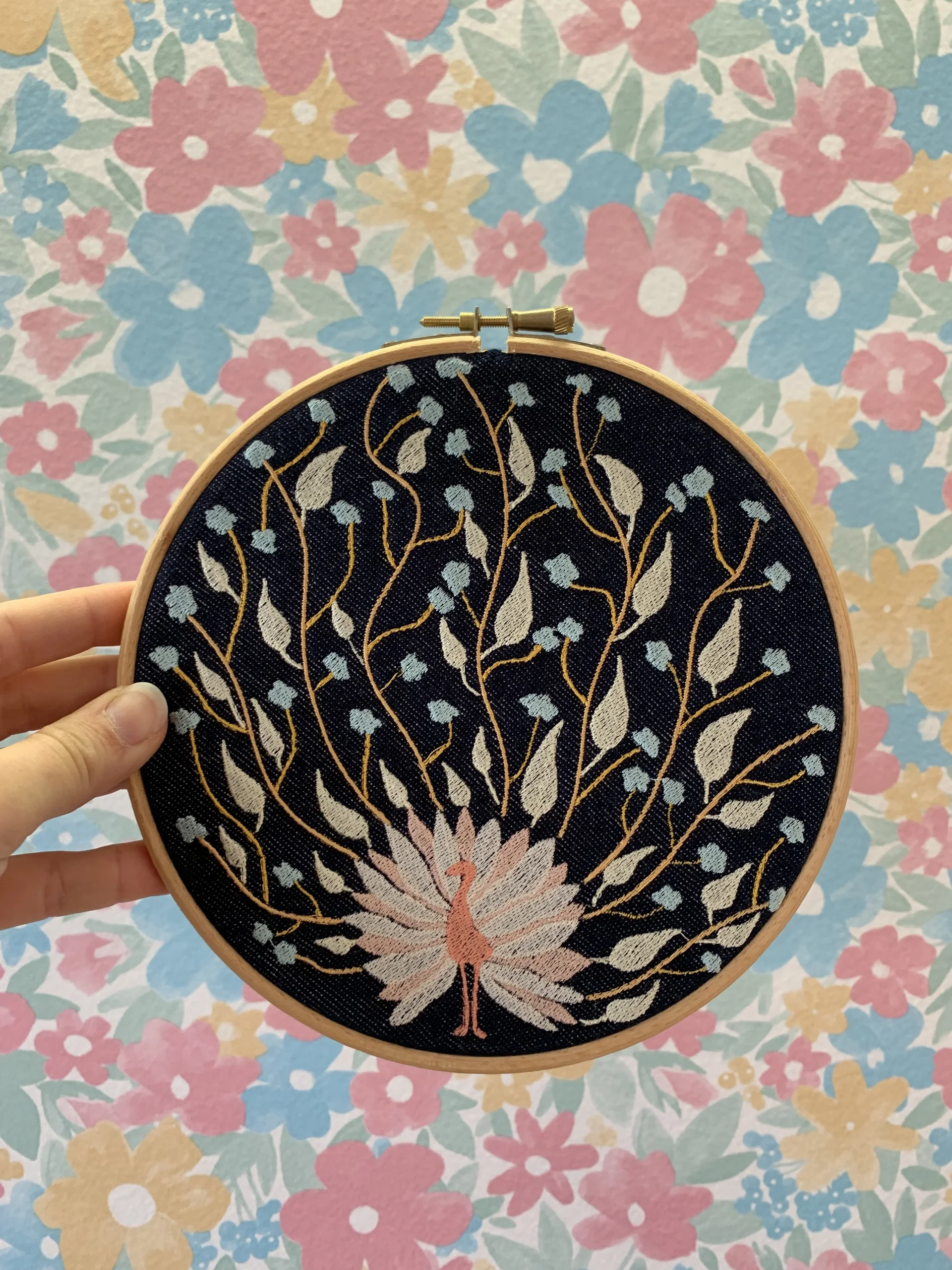 Décoration intérieure en textile, avec un motif brodé d'un paon dont les plumes sont devenus des feuilles et des fleurs