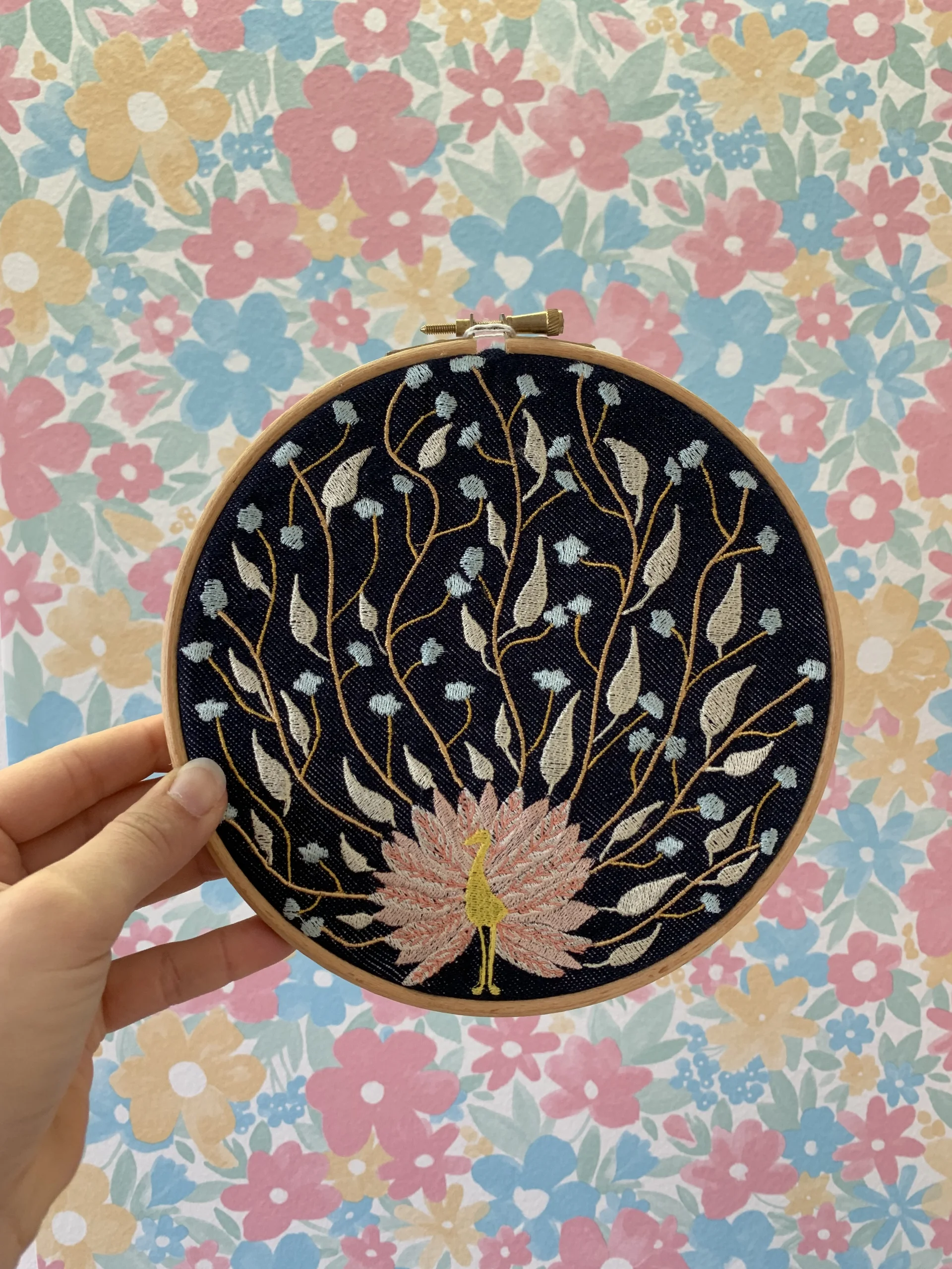Broderie d'une paon avec des feuilles et des fleurs à la place des ses plumes, sur un support en bois pour une décoration intérieure