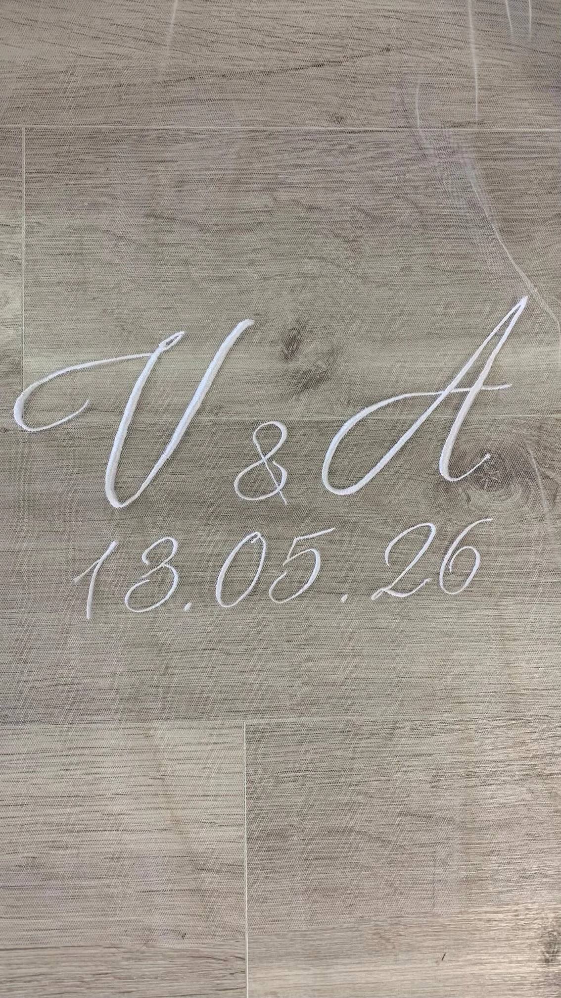 Gros plan d'initiales des futurs mariées ainsi que la date de mariage sur un voile en tulle