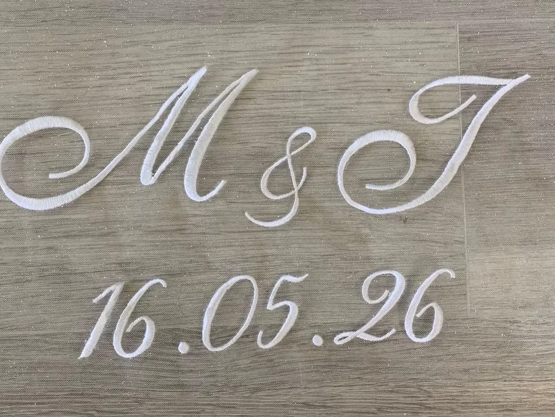 Gros plan d'initiales des futurs mariés ainsi que la date du mariage faite sur un voile de mariée