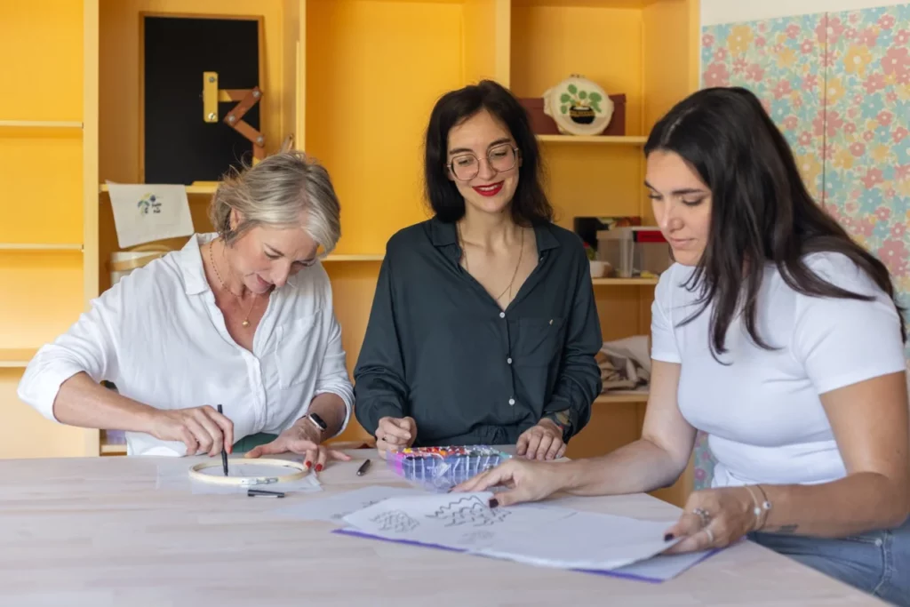 Julie artisane brodeuse accompagnant deux participantes lors d'une séance d'initiation à la broderie main