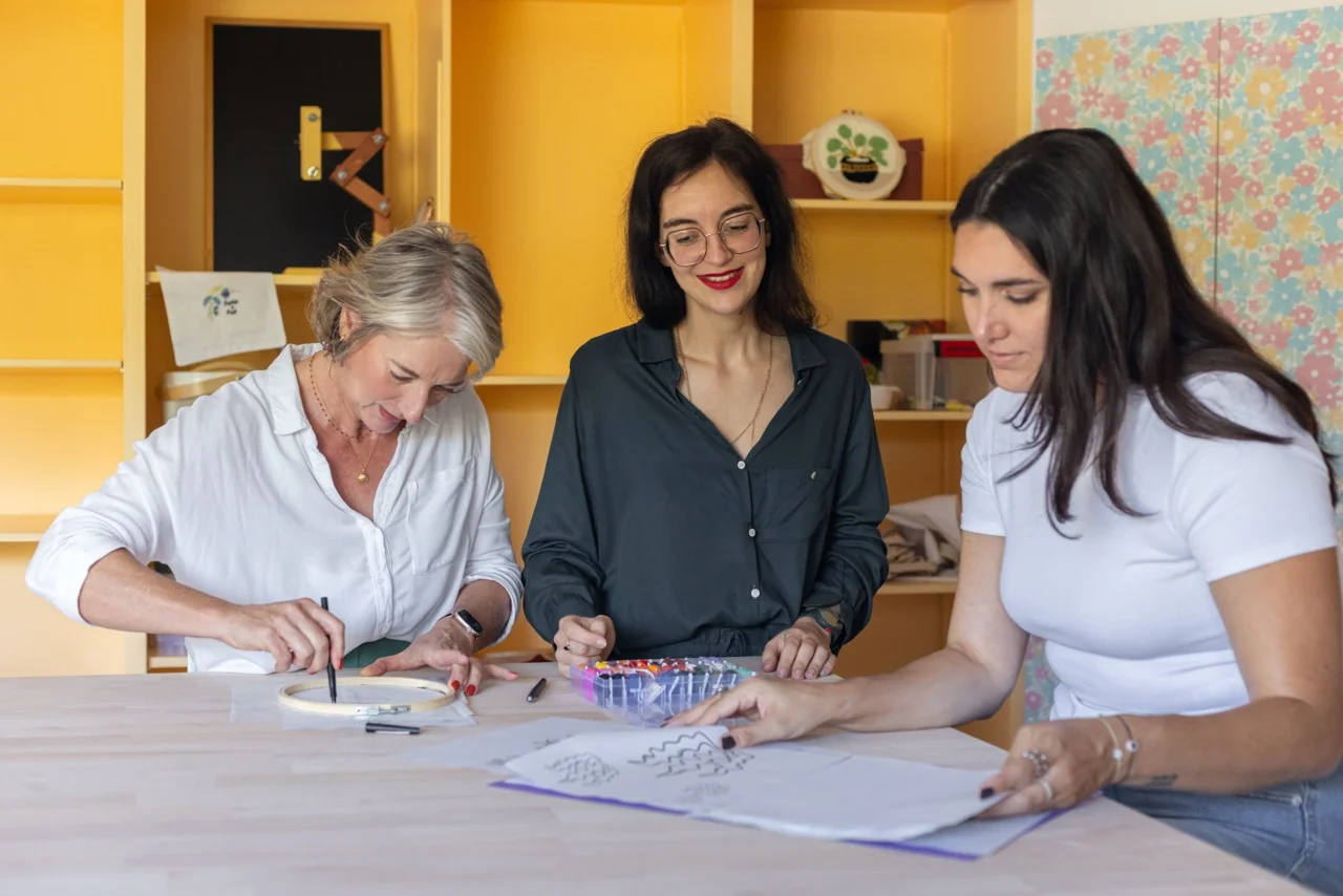 Julie artisane brodeuse accompagnant deux participantes lors d'une séance d'initiation à la broderie main