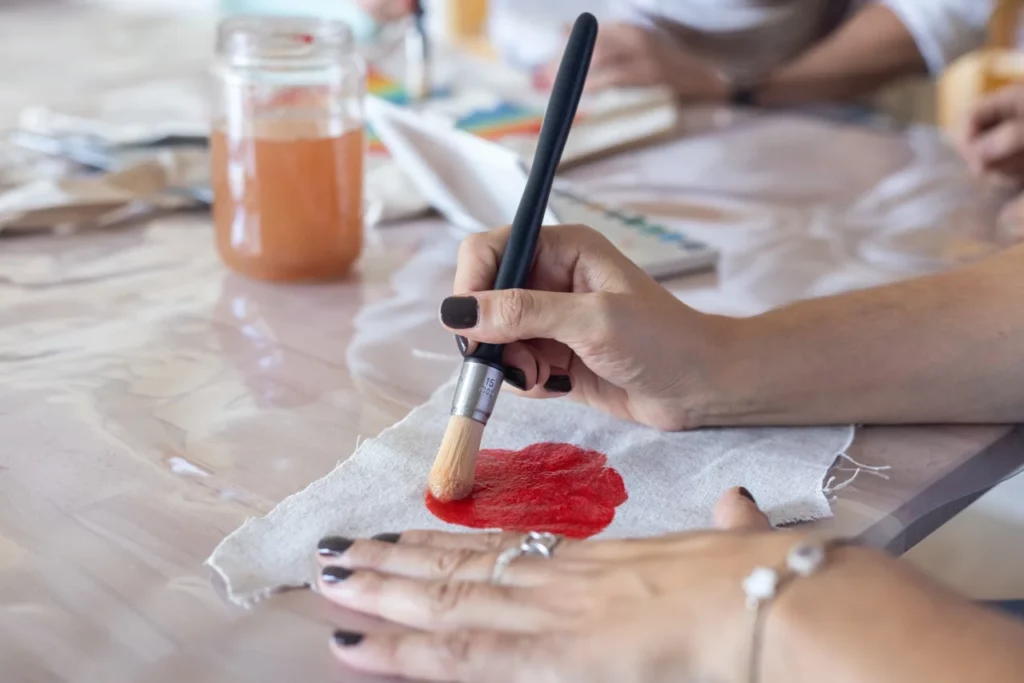 Main en train de faire un essai en aquarelle sur un textile en coton lors d'un atelier d'initiation à l'aquarelle et broderie main