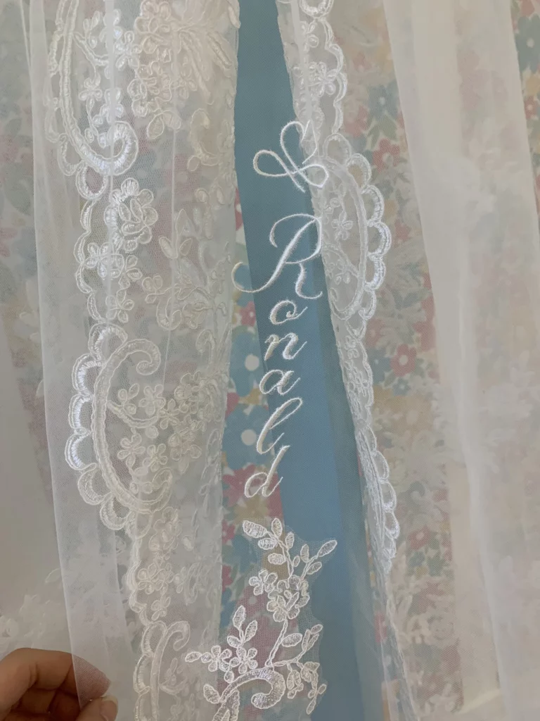 Gros plan d'une broderie de prénom sur un voile de mariée avec beaucoup de dentelles déjà présentes