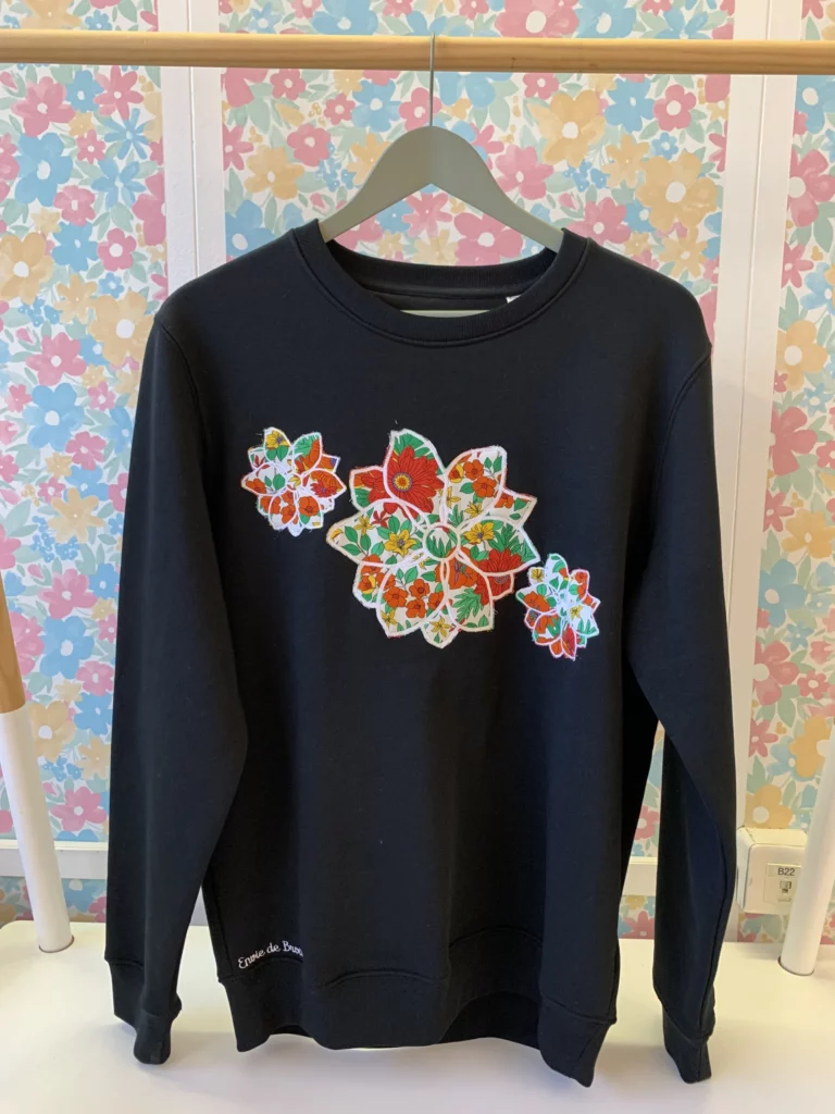 Vue de face du sweat-shirt noir brodé de trois grosses fleurs, dont l'intérieur de la broderie contient du tissu rouge et blanc très fleuris
