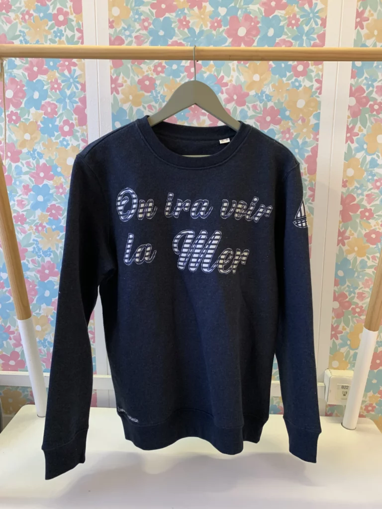 Vue de face du sweat-shirt en pièce unique brodé "on ira voir la mer" dont l'intérieur des lettres contient un tissu en marinière