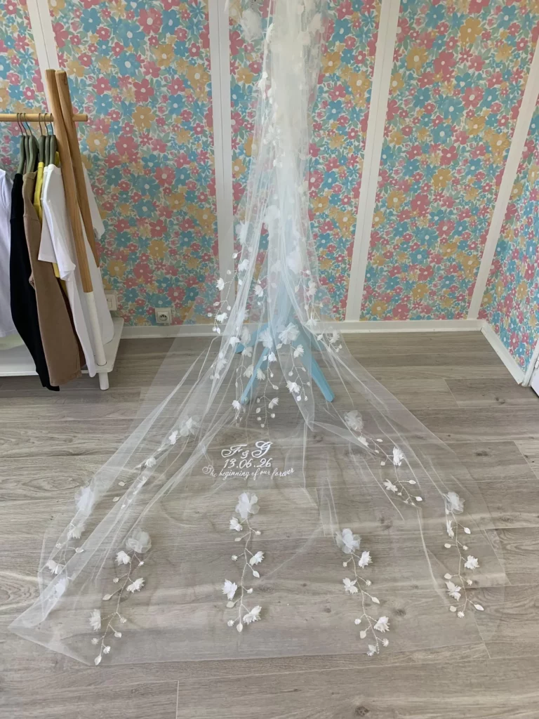 Voile de mariée brodée avec des initiales, la date du mariage ainsi q'une citation, vue en entier, avec déjà présent des fleurs en tissus